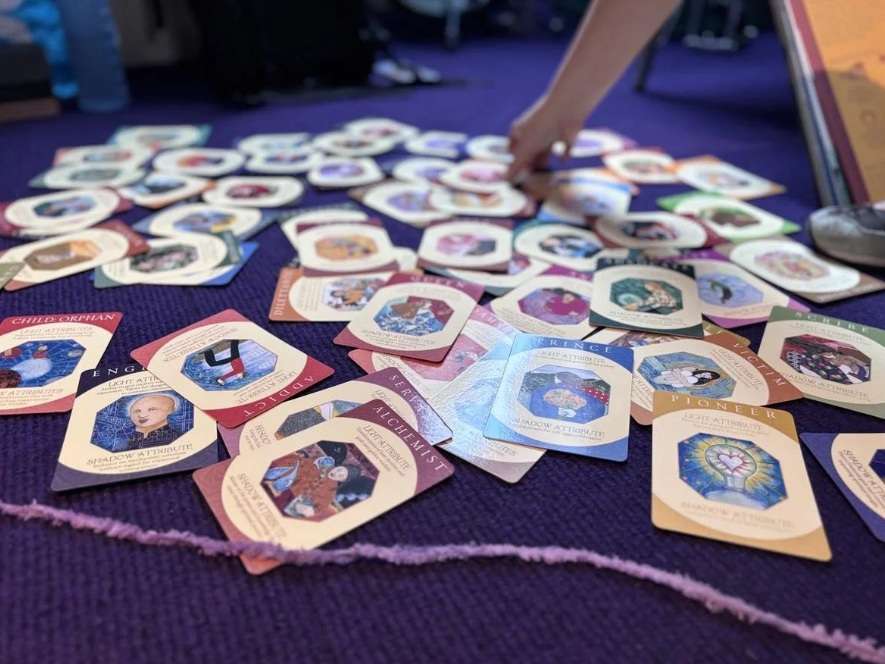 Tarot cards scattered across a blue textile surface, with a hand reaching in to take one.