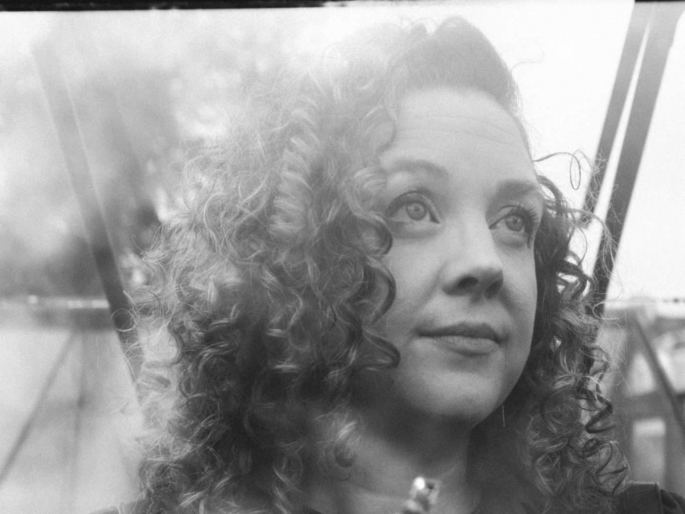 Black and white image of woman with dark curly hair holding a miniature house