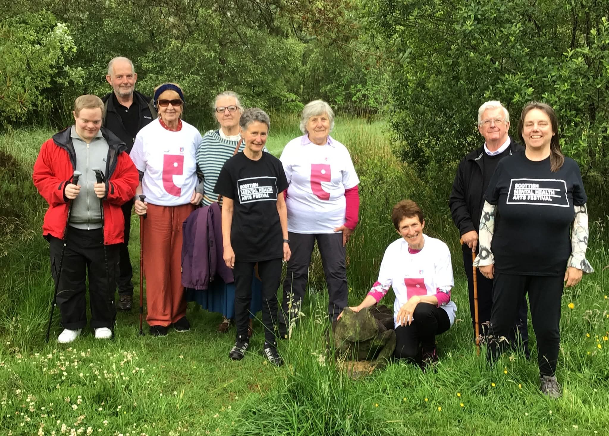 A group of nine people, some wearing SMHAF T-shirts, stand in a meadow.